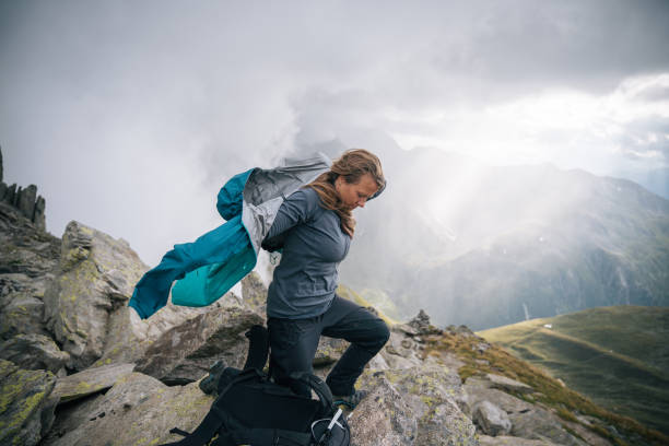 Woman mountaineer puts protective gear on, mountain ridge