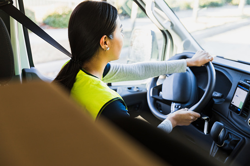 Using the navigation app on her smart phone, the young adult female delivery person drives to the next stop.