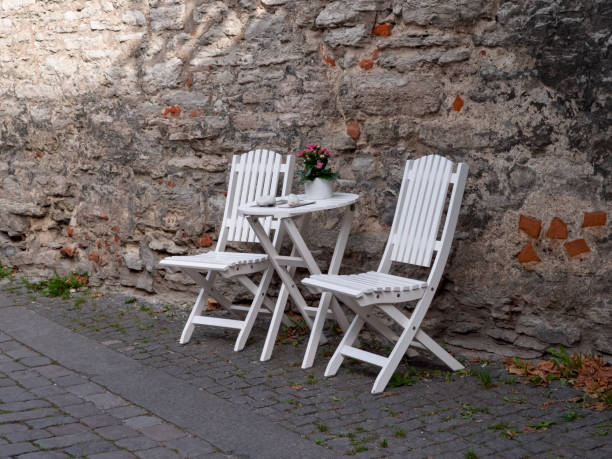 Two white wooden folding chairs with table invite you to rest in an alley