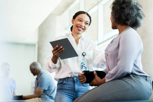 Physical therapist prepares to work with patient A confident young adult female therapist smiles at a patient before they begin a physical therapy session. The physical therapist is holding a digital tablet containing the patient's chart. doctor lifestyle stock pictures, royalty-free photos & images