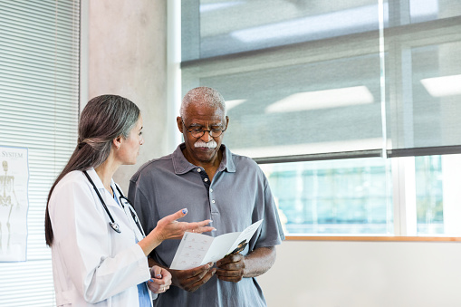 A mid adult female doctor gestures as she discusses home healthcare options with a senior adult male patient. The man is reading a home healthcare informational brochure.