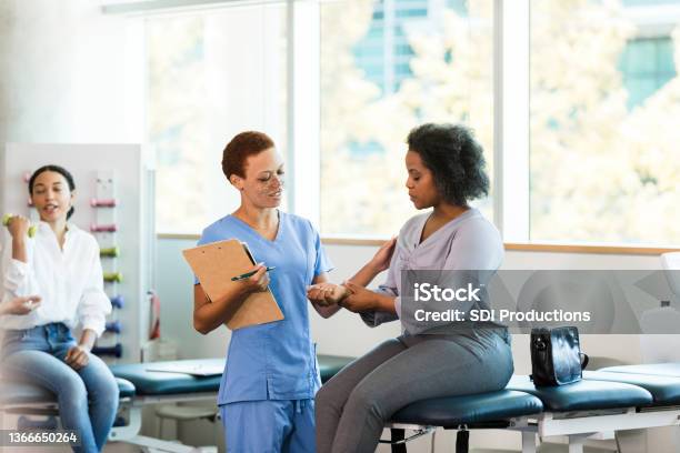 Female Occupational Therapist Asks Businesswoman About Wrist Pain Stock Photo - Download Image Now