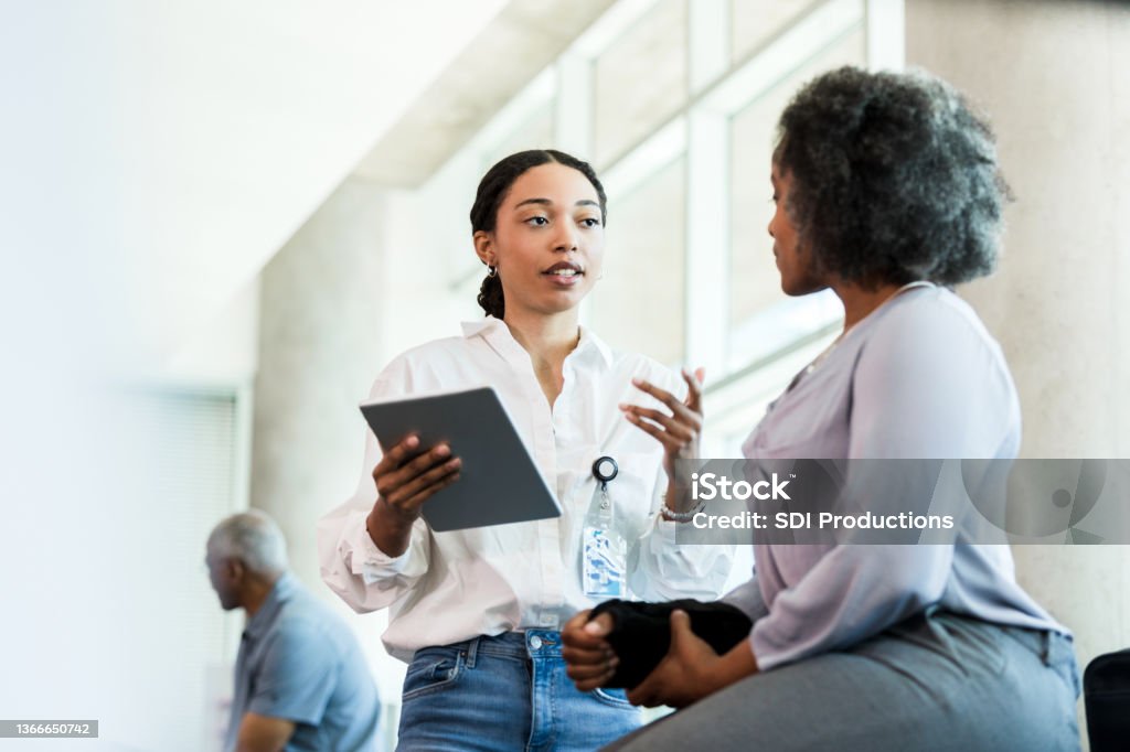 Physical therapist gestures while asking woman questions about injury The female young adult physical therapist gestures as she asks her mid adult patient questions about her injured wrist. Healthcare And Medicine Stock Photo
