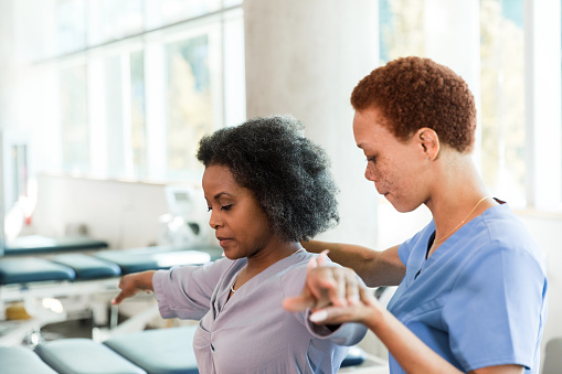 The mid adult woman concentrates as she learns arm and shoulder stretches from the female mid adult physical therapist.