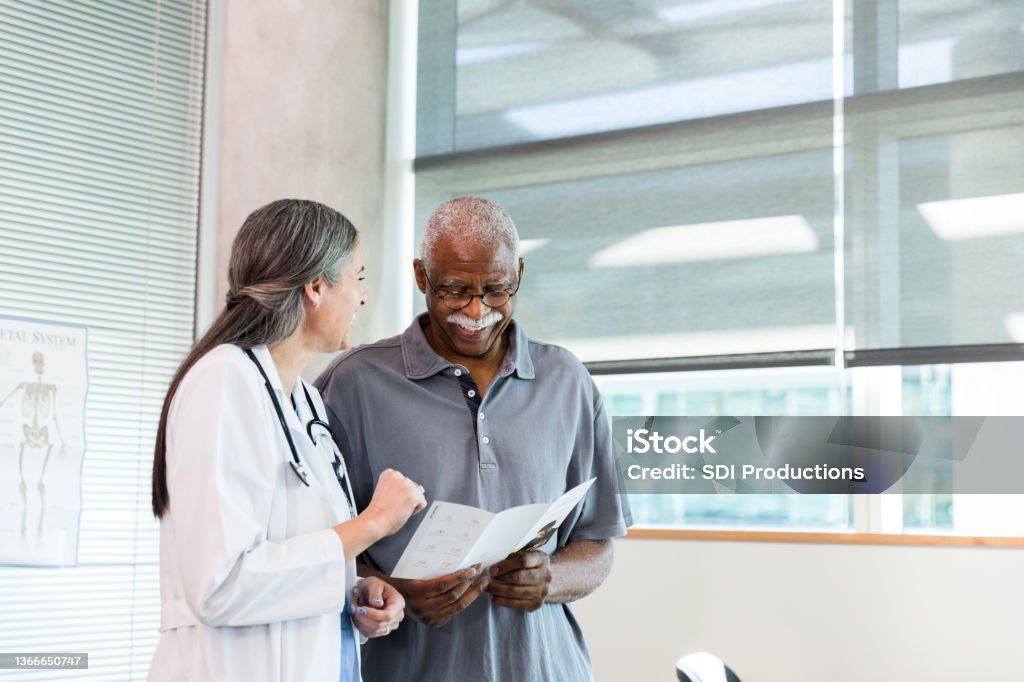 Orthopedic doctor and senior patient smile while discussing brochure information The female mid adult orthopedic doctor and the male senior adult patient smile as they discuss the information in the brochure. Patient Stock Photo