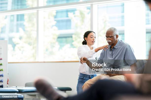 Physical therapist examines senior man's shoulder