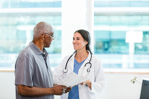 The mid adult female doctor and her senior adult male patient discuss the home healthcare options listed in the brochure.