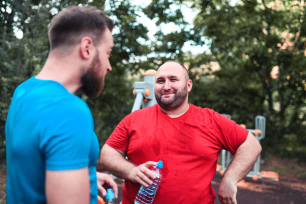 トレーニング後にフィットネスインストラクターと話す笑顔の太りすぎの男性 - crossfit exercising sports training outdoors ストックフォトと画像