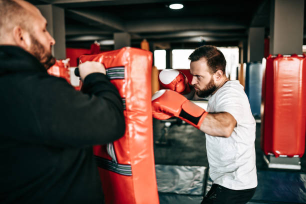 istock Determined Male Boxer Punching Training Pad With Coach Behind It 1366654252