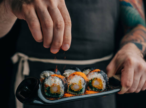 istock Man sprinkles spices on sushi rolls to serve the dish. 1366655929