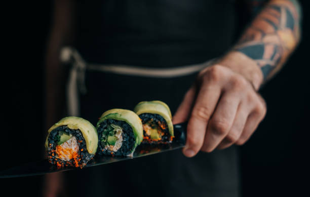 istock Man chef holds sushi rolls on a knife. 1366655944