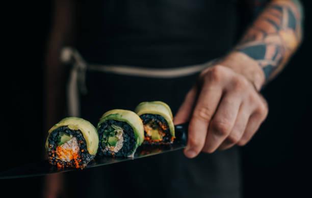 Man chef holds sushi rolls on a knife. stock photo