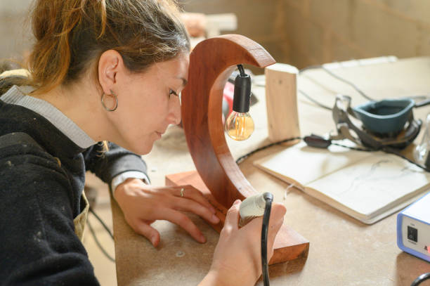 istock Beautiful young craftswoman engraving on handmade wooden lamp while using professional instrument. 1366659331