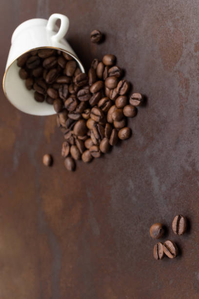 istock Roasted coffee beans are scattered from black cup onto table. 1366659789