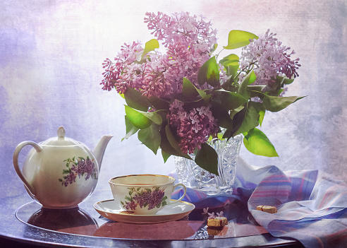 Spring tea party. A teapot, a cup, sweets and lilac flowers. Photo still life, stylization for painting, soft focus and toning