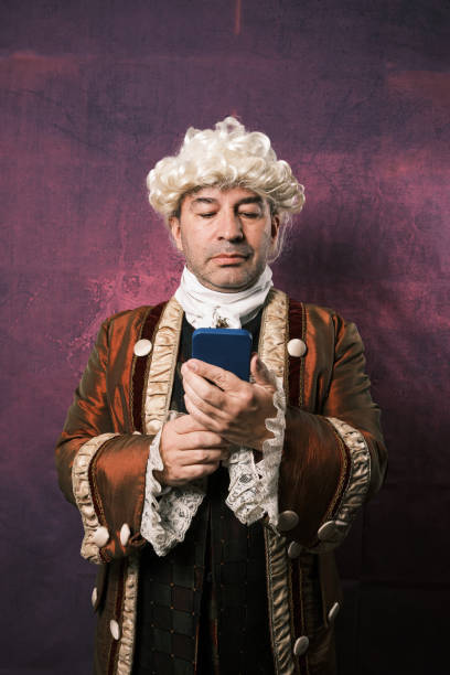 istock Man in classical renaissance clothes using a mobile phone while standing on an isolated background. 1366662928