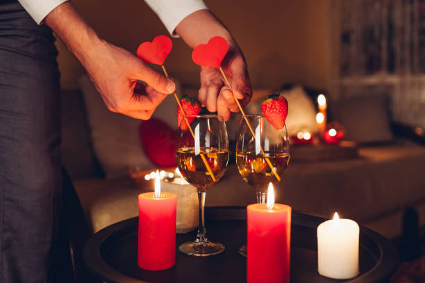 istock Man decorating table setting for Valentines day celebration at home putting hearts in glasses with champagne by candles 1366663588