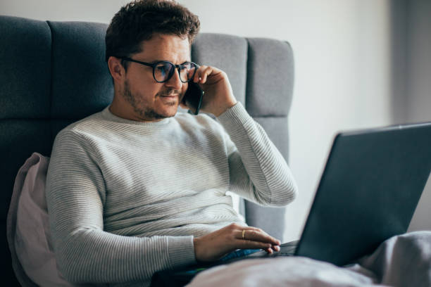istock Man with glasses talking on the phone and checking emails from laptop 1366666740