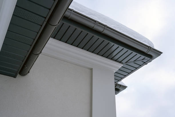 Corner of the house with new gray metal tile roof and rain gutter covered by snow at winter. Metallic Guttering System, Guttering and Drainage Pipe Exterior stock photo