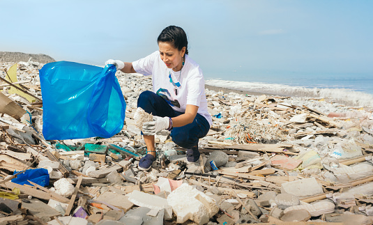 A woman picks up trash on a beach. Copy space