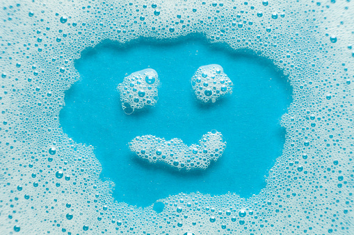 House cleaning. Smiley from foam detergent on a blue background. Soap suds and bubbles.