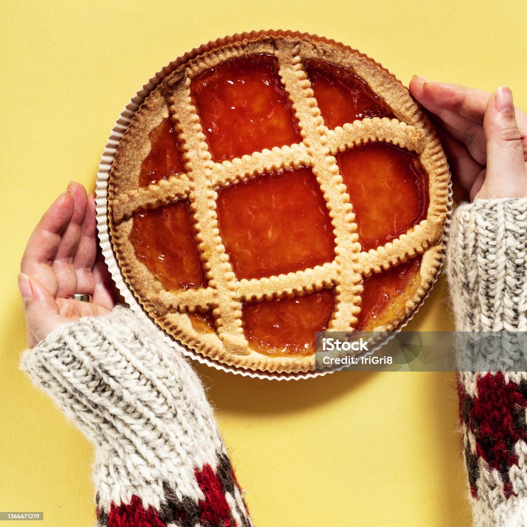italian crostat pie with apricot jam on a yellow background and female hands in a warm woolen sweater with an ornament Crostata Stock Photo