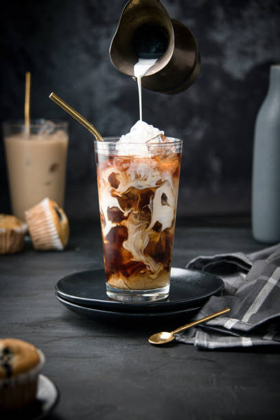Glass with ice and coffee A glass filled up with cubes of ice on black background and hand pouring dark coffee on it iced coffee stock pictures, royalty-free photos & images
