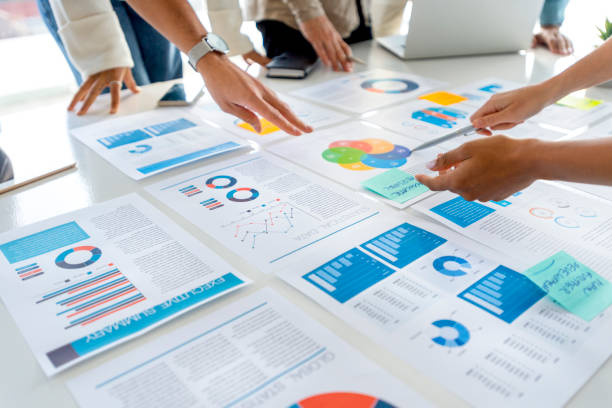 istock Paperwork and hands on a board room table at a business presentation or seminar. 1366672573