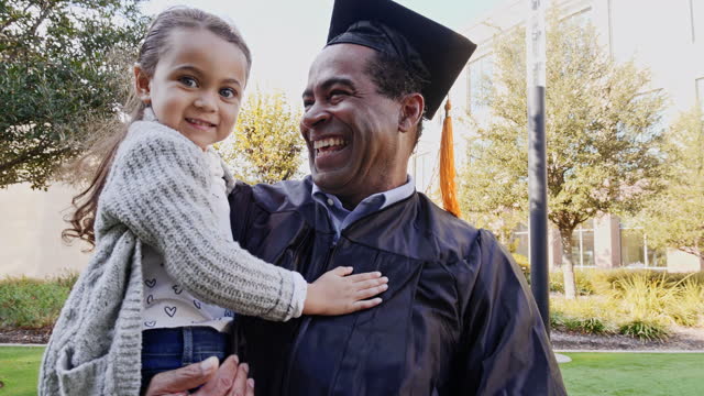 A happy little girl runs into her grandpa's arms after his college graduation. She turns around and smiles.