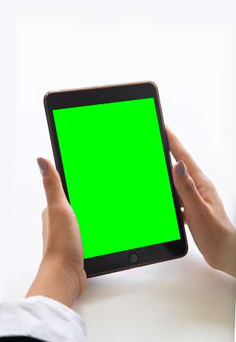 The photo includes two hands of a woman holding the smart tablet for examining the recent data of the corporate. She is the tank, thinking about what should be the strategy for the company in long term. This photo is a representation of the businesswoman. The screen of the smart tablet is also a template, chroma key on which one can customize. The concept of this photo is a green screen, blank background, office desk, and occupation.  chrome key.