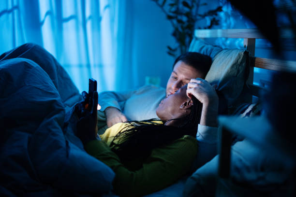 istock Cuddling couple looking at smartphone together while laying in bed during night 1366675091