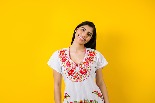 portrait of young latin woman with mexican dress and copy space on yellow background in Latin America