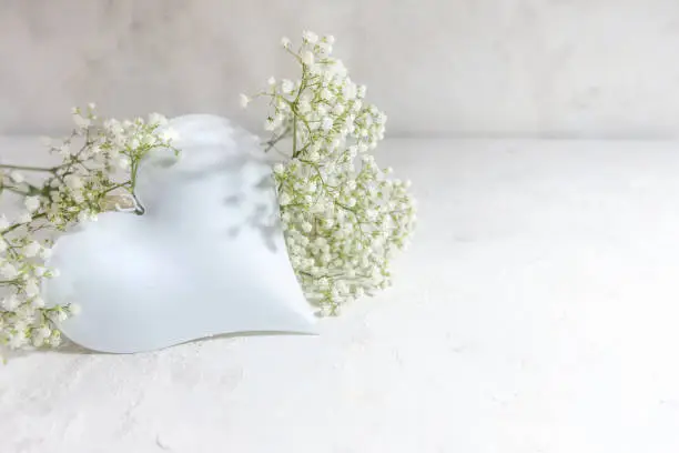 White colored heart shape with gypsophila flowers on a light background, love concept with large copy space, selected focus, narrow depth of field