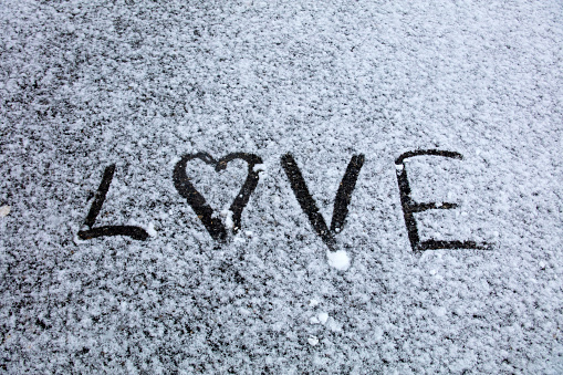 Two hearts (symbol of love) hand drawing (painted) on snow on the glass above windshield wiper of a car. Valentine's Day, love, honeymoon, winter, transport concept. Copy space. Selective focus.