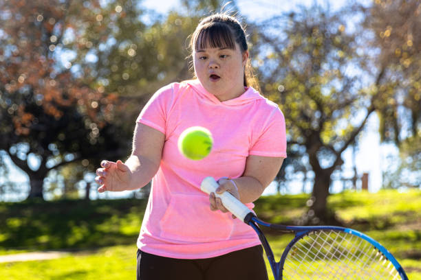 Girl with Down's Syndrome Playing Tennis A girl with Down’s Syndrome playing Tennis outdoors wheelchair tennis stock pictures, royalty-free photos & images