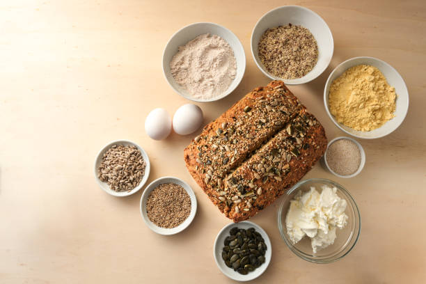 Low carb whole grain bread with seeds surrounded by the ingredients on a wooden table, baking at home and healthy eating concept, copy space, high angle view from above, selected focus