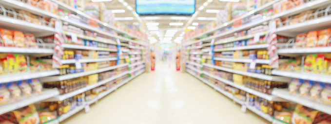 Close up color image depicting a sign with the word 'snacks' in a supermarket aisle. Focus on the sign with the snacks on the shelves defocused beyond. Room for copy space.