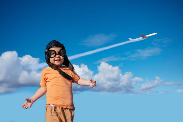Little toddler boy in aviator hat and googles smiling, over commercial jet plane in the sky
