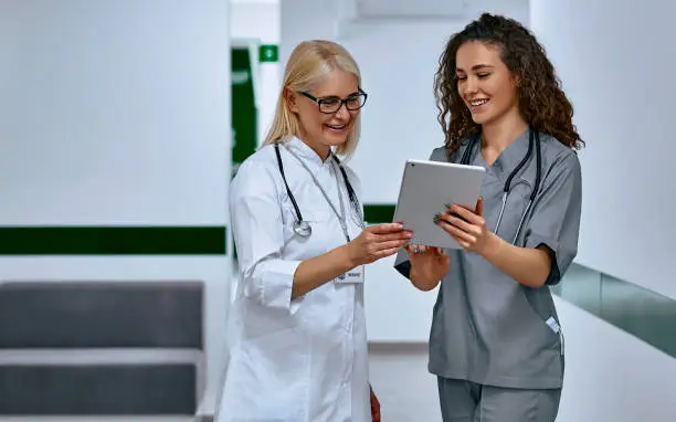 Photo of Doctors laugh and talk in the hallway. Older woman and young female doctors.