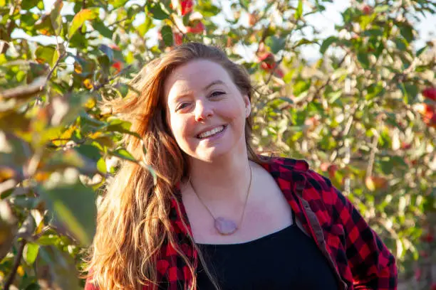 beautiful woman with a lovely smile and red hair grins in her apple orchard