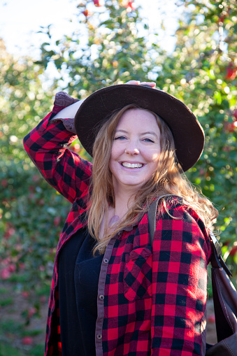 beautiful relaxed woman in plaid and a hat explores the world in an apple orchard