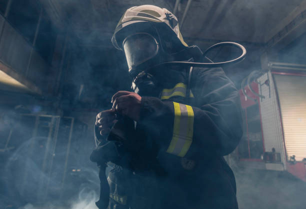 retrato de um bombeiro usando bombeiros usando máscara de oxigênio. fundo escuro com fumaça e luz azul. - turnouts - fotografias e filmes do acervo