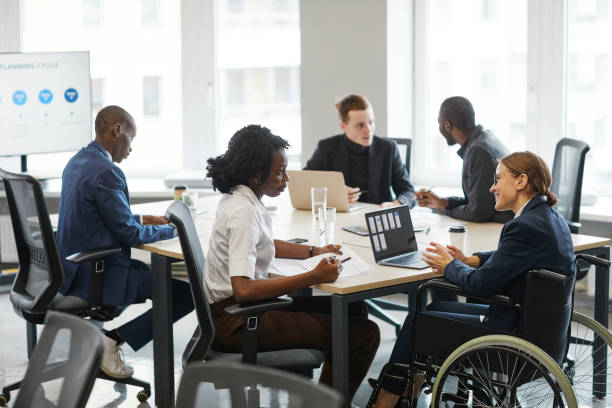 Smiling Businesswoman using Wheelchair in Meeting Portrait of successful businesswoman using wheelchair while speaking to employee in meeting, copy space accessibility stock pictures, royalty-free photos & images