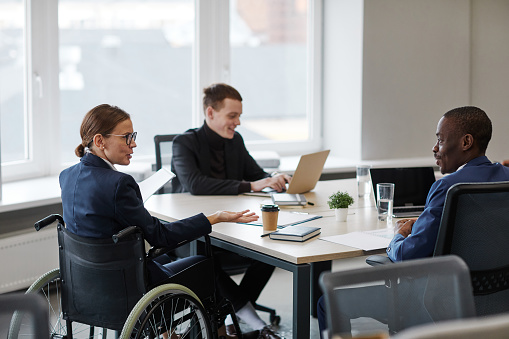 Back view portrait of successful businesswoman using wheelchair while leading board meeting in office, copy space