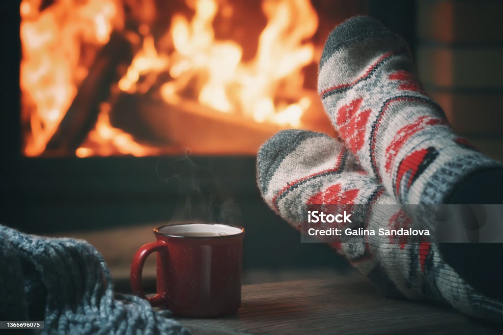 Girl resting and warming her feet by a burning fireplace in a country house on a winter evening. Selective focus Girl resting and warming her feet by a burning fireplace in a country house on a winter evening. Selective focus. Winter Stock Photo