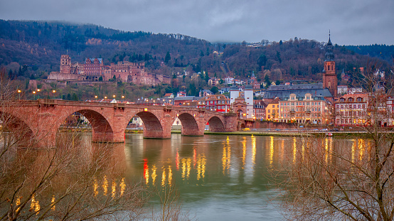 A view of Heidelberg, Germany and the Old Bridge from across the Neckar River in twilight with lights reflecting off of the water.