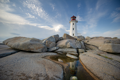 The lighthouse at Peggy's Cove, a Canadian Federal Heritage Building, reflecting on a puddle between rocks. Nova Scotia, Canada