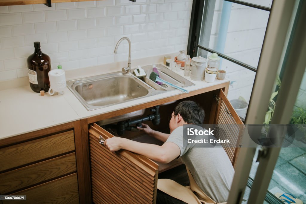 Southeast Asian repairman working in the kitchen skill, expertise, looking, repairing, fixing, drain, pipe, kitchen sink Leaking Stock Photo