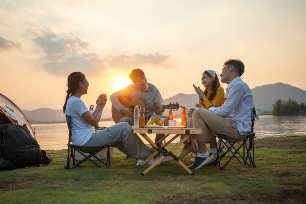 happy group of Asian friends Play guitar and sing enjoying camping and drinking beer stock photo
