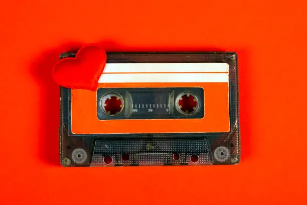 Old Audio Cassette with a Red Heart on the Red Paper Background closeup